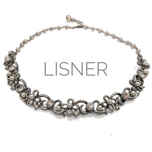 Puede incluir: Collar Lisner plateado con diseño floral y de volutas. El collar presenta perlas de imitación y pedrería transparente. La palabra "LISNER" está impresa en el centro de la imagen.