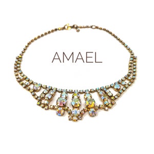 May include: A gold necklace featuring iridescent rhinestones. The necklace has a delicate chain and a cascading design of stones. The word "AMAEL" is written in the centre of the image.