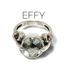 May include: A silver ring with a large, round, light green gemstone set in a silver setting. The ring has two gold accents on either side of the stone. The ring is marked "10K" and "EFFY" on the band.
