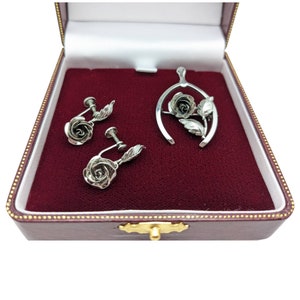 May include: A set of silver rose jewellery in a red velvet box. The set includes a pendant necklace and a pair of earrings.