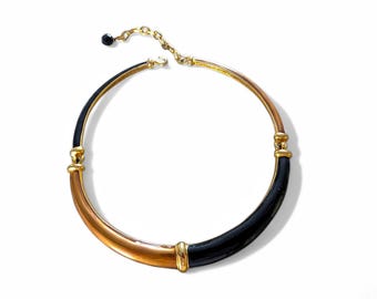 May include: A gold and black choker necklace with a simple design. The necklace is made of metal and has a smooth finish.