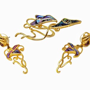 Könnte beinhalten: Ein Set aus goldfarbenen Ohrringen und einer Brosche mit einem floralen Design mit schillernden Abalone-Muschelakzenten. Die Ohrringe sind im Hänge-Stil und die Brosche hat eine Stecknadel.