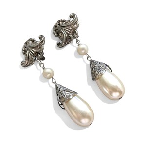 Peut inclure: Une paire de boucles d'oreilles pendantes vintage. Les boucles d'oreilles présentent des accents filigranés argentés ornés et des fausses perles en forme de poire. Design classique et élégant, idéal pour les occasions spéciales.