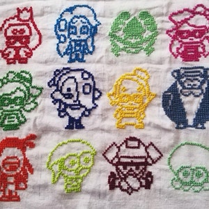 May include: A white fabric with 10 colorful embroidered characters. The characters are in a grid pattern and are all different colors. The characters are all wearing different outfits and have different expressions.