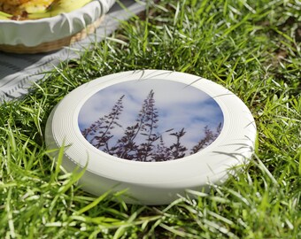May include: White plastic frisbee with a printed image of tall grass and a blue sky with clouds.