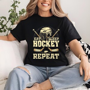 May include: Black t-shirt with a hockey helmet and sticks graphic. The text on the shirt reads "Eat Sleep Hockey Repeat".