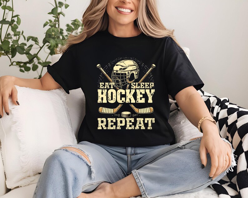 May include: Black t-shirt with a hockey helmet and sticks graphic. The text on the shirt reads "Eat Sleep Hockey Repeat".