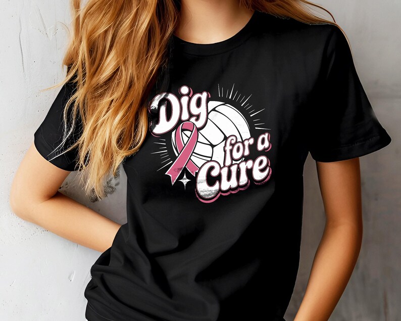 May include: Black t-shirt featuring a volleyball with a pink ribbon and the text "Dig for a Cure" in white and pink. The design includes a star and radiating lines, symbolizing support for a cause. The shirt is a classic crew neck style.