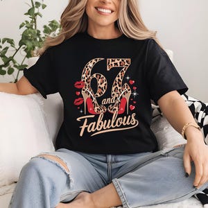 May include: Black t-shirt with a leopard print number 67 and the words "and fabulous" in gold lettering. The number 67 is decorated with red high heels.