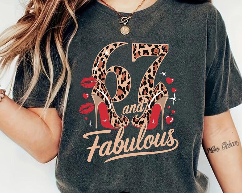May include: A dark gray t-shirt with a leopard print design featuring the numbers "67" and the words "and fabulous". The numbers are decorated with red high heels.