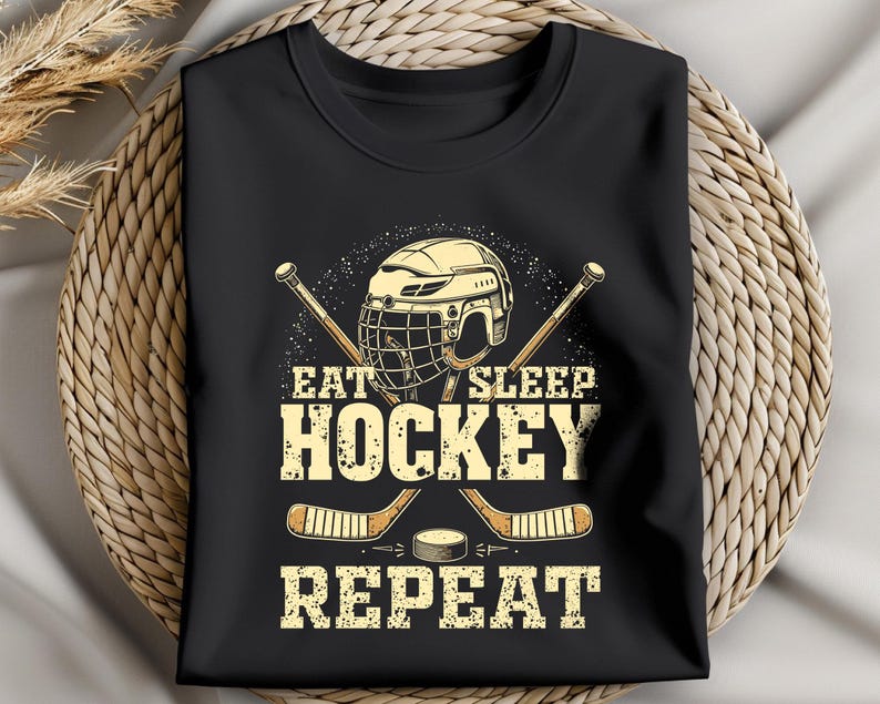 May include: Black t-shirt featuring a hockey helmet, sticks, and puck graphic. The text reads "Eat Sleep Hockey Repeat".