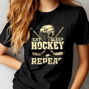 May include: Black t-shirt featuring a hockey stick and helmet graphic. The text on the shirt reads "Eat Sleep Hockey Repeat."