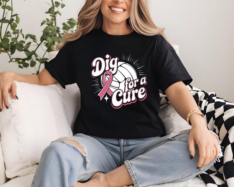 May include: Black t-shirt with the text "Dig for a Cure" in white and pink, featuring a volleyball and a pink ribbon. The shirt is worn with blue jeans.