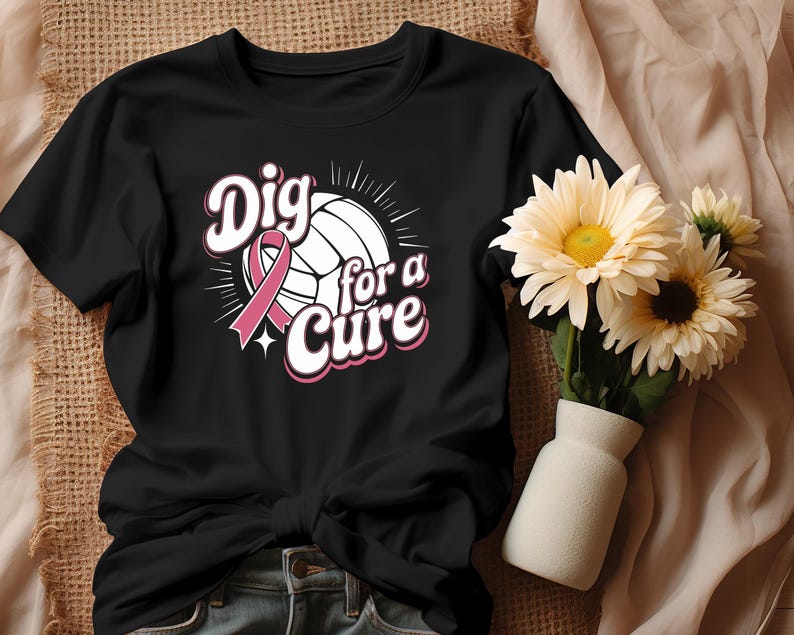 May include: Black t-shirt featuring a volleyball with a pink ribbon and the text "Dig for a Cure" in a pink and white design. The shirt is a crew neck style and is knotted at the waist. A vase of flowers is in the background.