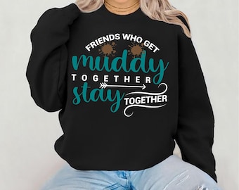 May include: Black sweatshirt with the text "FRIENDS WHO GET MUDDY TOGETHER STAY TOGETHER" in white and teal lettering. The sweatshirt has a crew neck and long sleeves. The model is wearing blue jeans.