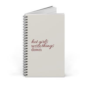 Könnte beinhalten: Ein spiralgebundenes Notizbuch mit hellgrauem Einband und dem dunkelroten Text "hot girls write things down" auf der Vorderseite. Das Notizbuch hat eine schwarze Metallspirale an der linken Seite und ist oben leicht geöffnet dargestellt.