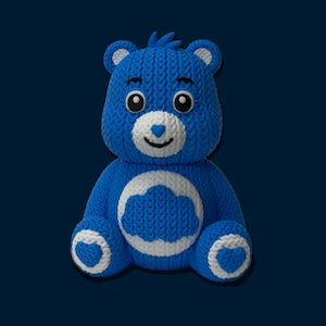 May include: A blue knitted teddy bear with white accents. The bear has a white cloud design on its belly, white hearts on its feet, and a white heart on its nose. The bear has black eyes and a smiling face.