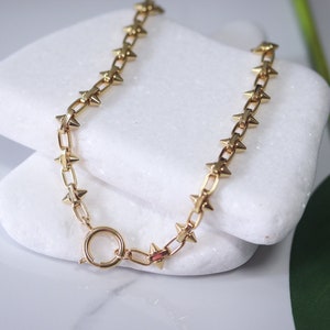 May include: A gold chain necklace with star-shaped spikes. The necklace is on a white surface.