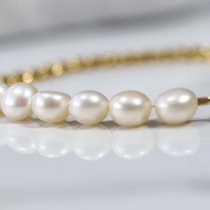 May include: A gold chain bracelet with a row of white pearls. The bracelet has a clasp closure.