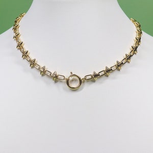 May include: A gold chain necklace with a series of small, pointed spikes. The necklace has a simple, round clasp.