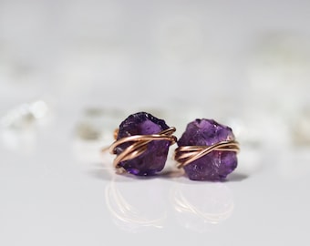 May include: A pair of amethyst earrings with rose gold wire wrapping. The amethyst stones are raw and have a natural, irregular shape.