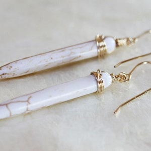 May include: A pair of white, long, pointed earrings with gold wire wrapped around the top of each earring.