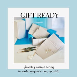 May include: Gift ready jewelry packaging with a necklace, earrings, and a pair of earrings in a small white pouch. The jewelry is displayed on a white surface with a blue background.