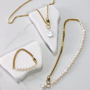 May include: Three gold necklaces with pearl accents. One necklace features a single large pearl pendant, another has a row of smaller pearls, and the third is a simple chain with a small pearl pendant.