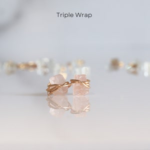 K&ouml;nnte beinhalten: Ein Paar golddrahtgewickelte Ohrringe aus rosa Kristall. Die Kristalle sind dreimal mit Golddraht umwickelt. Die Ohrringe liegen auf einer wei&szlig;en Oberfl&auml;che.