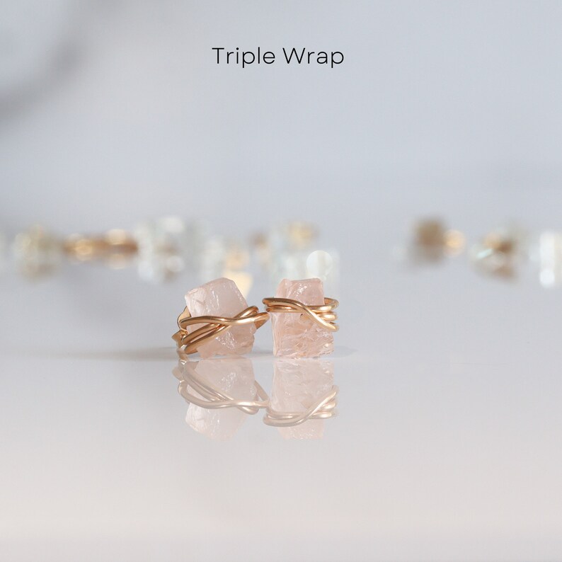 K&ouml;nnte beinhalten: Ein Paar golddrahtgewickelte Ohrringe aus rosa Kristall. Die Kristalle sind dreimal mit Golddraht umwickelt. Die Ohrringe liegen auf einer wei&szlig;en Oberfl&auml;che.