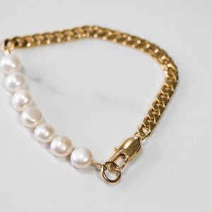 May include: A gold chain bracelet with a row of white pearls. The bracelet has a lobster clasp closure.