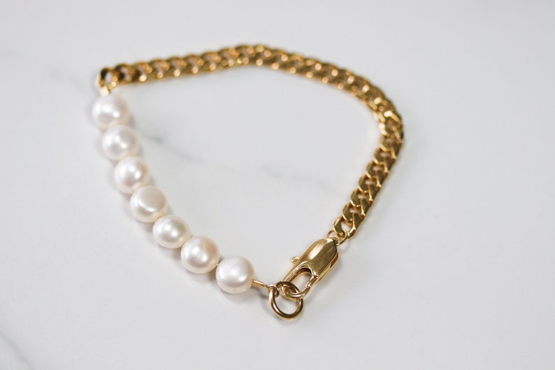 May include: A gold chain bracelet with a row of white pearls. The bracelet has a lobster clasp closure.