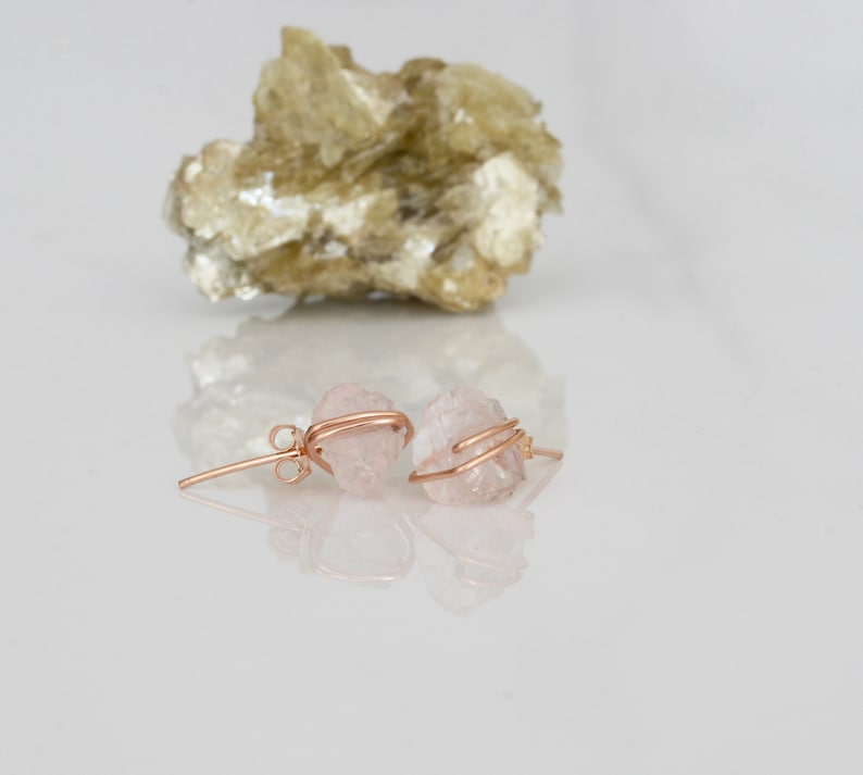 K&ouml;nnte beinhalten: Ein Paar Ohrringe aus Rosenquarz mit einer rohen, nat&uuml;rlichen Kristallform. Die Ohrringe sind aus ros&eacute;goldfarbenem Draht gefertigt, der um die Kristalle gewickelt ist.