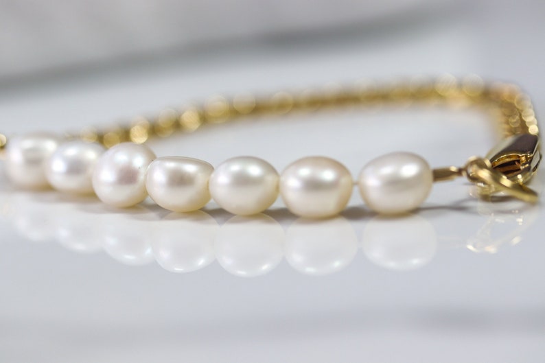 May include: A gold chain bracelet with a row of white pearls. The bracelet has a clasp closure.