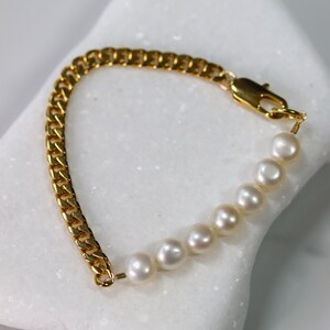 May include: A gold chain bracelet with a row of white pearls. The bracelet has a lobster clasp closure.