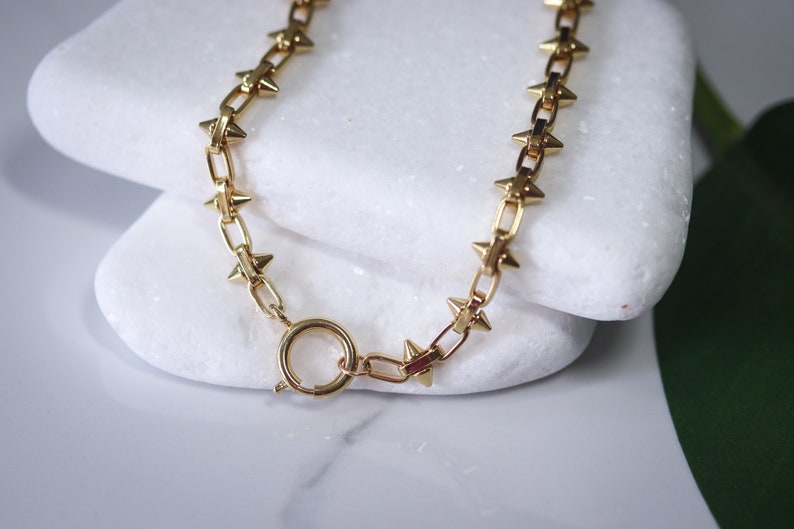 May include: A gold chain necklace with small, pointed spikes. The chain is linked together with a simple, round clasp.