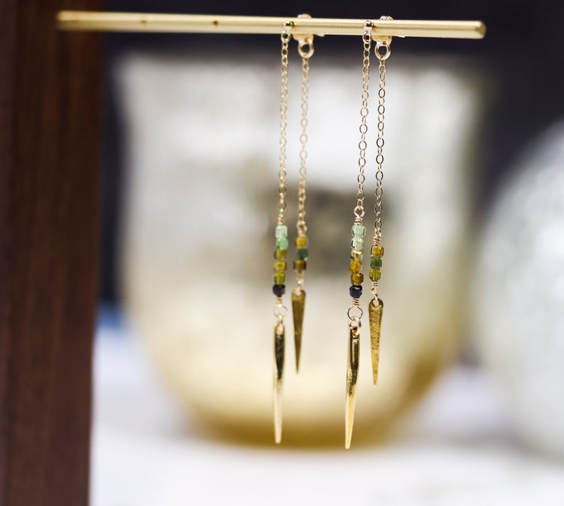 May include: Three pairs of gold earrings with green and black beads and a gold spike at the bottom.