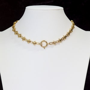 May include: A gold-toned choker necklace with a chain link design and pointed spikes. The necklace has a simple clasp closure.