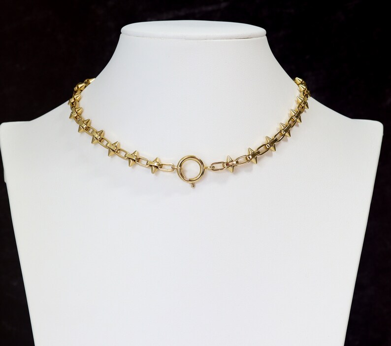 May include: A gold-toned choker necklace with a chain link design and pointed spikes. The necklace has a simple clasp closure.