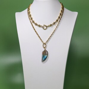 May include: A gold chain necklace with a large iridescent blue and brown stone pendant. The necklace is layered with a shorter chain with spikes.