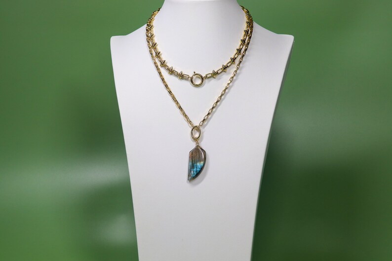 May include: A gold chain necklace with a large iridescent blue and brown stone pendant. The necklace is layered with a shorter chain with spikes.