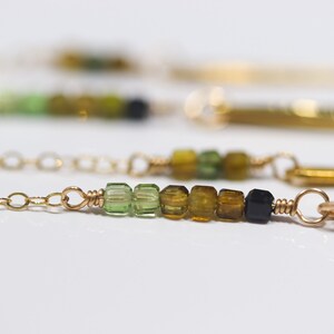 May include: A gold chain necklace with a bar pendant and a row of green, brown, and black gemstone beads.