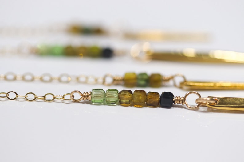 May include: A gold chain necklace with a bar pendant and a row of green, brown, and black gemstone beads.