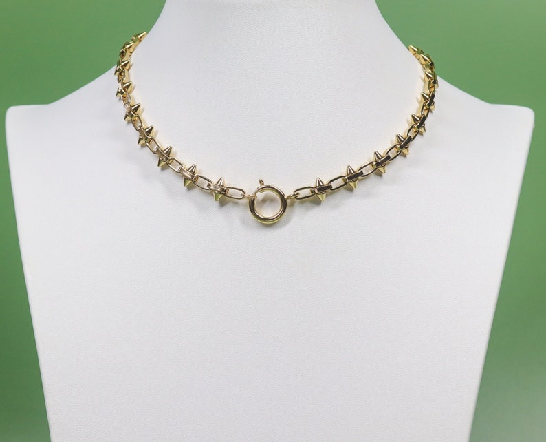 May include: A gold chain necklace with a series of small, pointed spikes. The necklace has a simple, round clasp.