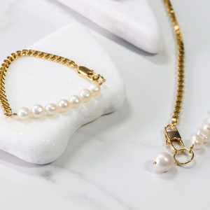 May include: A gold chain bracelet with a row of white pearls. The bracelet is on a white surface. A gold chain necklace with a row of white pearls is also pictured.