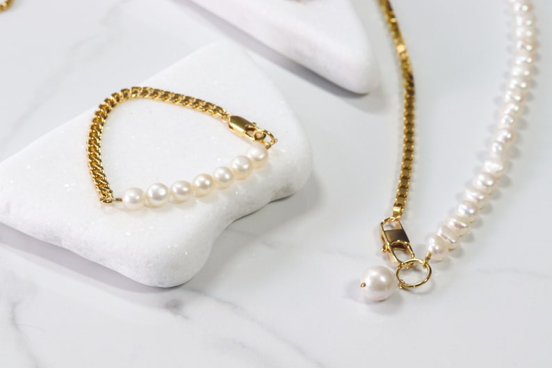 May include: A gold chain bracelet with a row of white pearls. The bracelet is on a white surface. A gold chain necklace with a row of white pearls is also pictured.