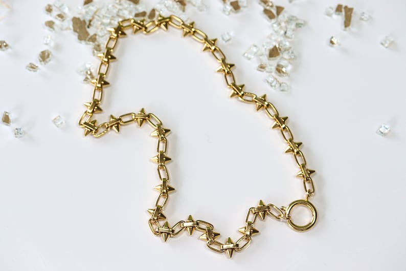 May include: A gold chain necklace with small, pointed spikes. The chain is linked together with a round clasp.