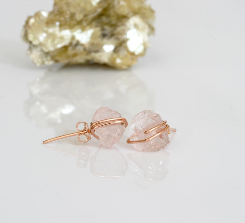 May include: A pair of rose quartz earrings with gold wire wrapping. The earrings are made with natural, raw rose quartz crystals. The rose quartz is a light pink color.