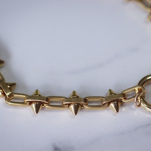 May include: A gold chain bracelet with a clasp and pointed spikes.