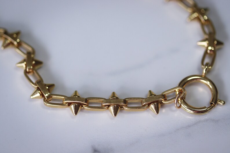 May include: A gold chain bracelet with a clasp and pointed spikes.